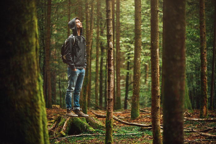 Why Being in Nature Is Good for You - young man in forest with hoodie and backpack