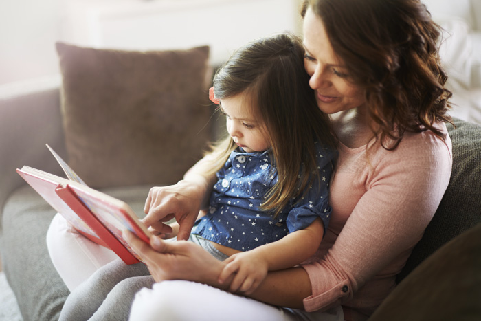 brunette woman with little girl on her lap reading a book together - children