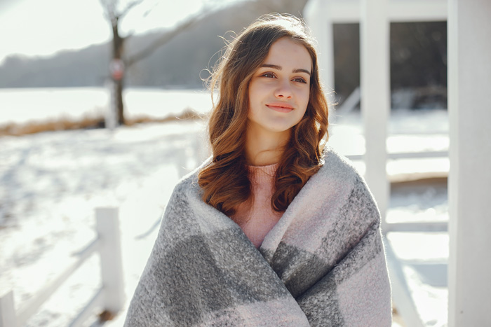 beautiful young woman wrapped in plaid blanket walking outside in the winter - seasonal affective disorder