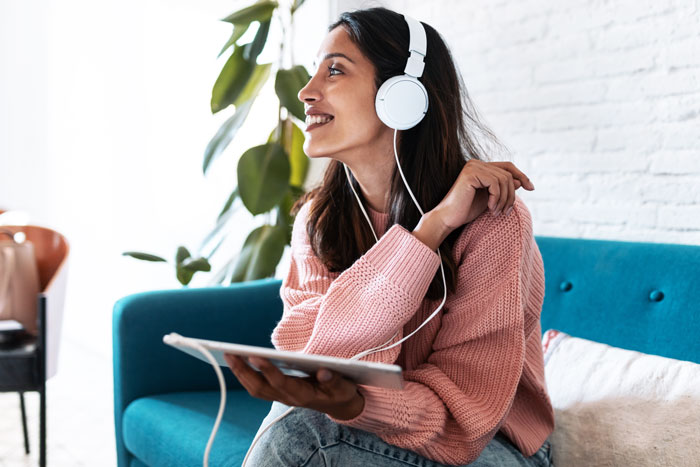 pretty smiling woman listening to headphones connected to tablet computer - podcasts