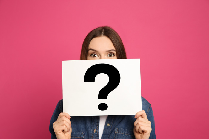 woman holding white sign with black question mark on it against pink background - willpower