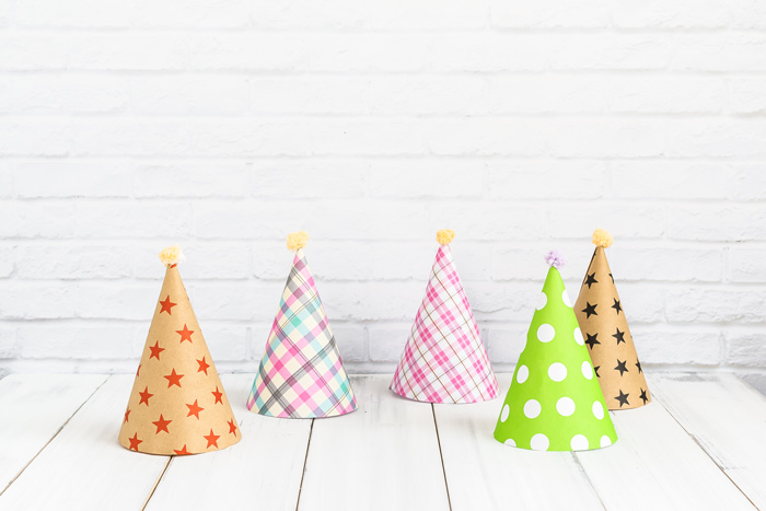 colorful paper party hats sitting on white wooden table - fun
