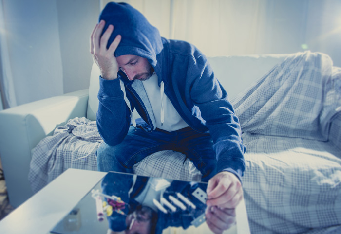 Understanding Drug and Alcohol Addiction, sad man in a hoodie cutting lines of cocaine on a table at home - cocaine addiction