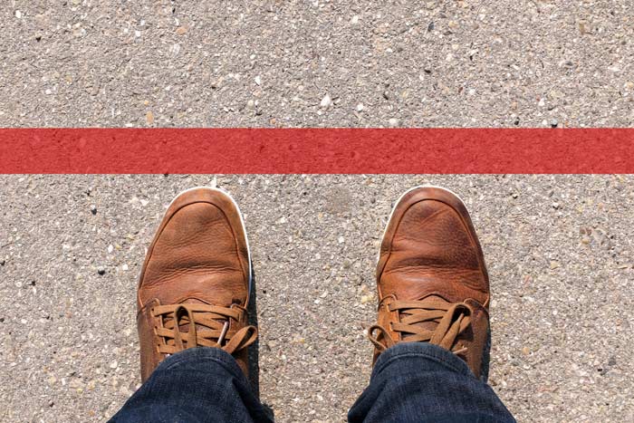 cropped shot of a person's shoed feet toed up to a red line on the concrete - boundaries