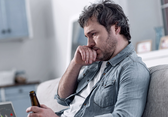 middle age man sitting at home on the couch drinking a bottled beer, looking rather unhealthy - health