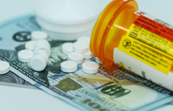 round white tablets spilling out of prescription bottle and onto a couple of one hundred dollar bills - oxycodone